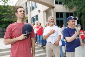 People wit hand over heart and hat in hand recite the Pledge of Allegiance