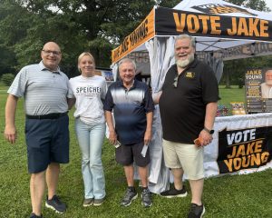 Rob Matzie, Sydney Speicher, Tony Amadio, Jake Young in front of a black and gold tent